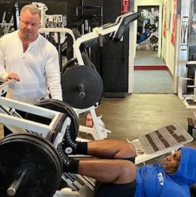 Man doing leg press in gym supervised by trainer.