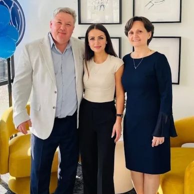 Three people posing together indoors with yellow sofas.
