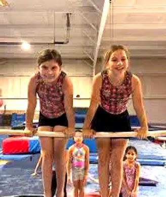 Two girls practicing gymnastics on parallel bars indoors.